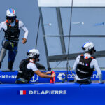 Manon Audinet, strategist of France SailGP Team, at the wheel as Quentin Delapierre, driver of France SailGP Team, runs across the boat during a practice session ahead of the ROCKWOOL Denmark Sail Grand Prix in Copenhagen, Denmark. 18th August 2022. Photo: Jon Buckle for SailGP. Handout image supplied by SailGP